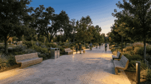 مسیر سنگفرش پارک در غروب با نیمکت های چوبی، چراغ های کوتاه بولارد و تردد عابران و دوچرخه سوارها