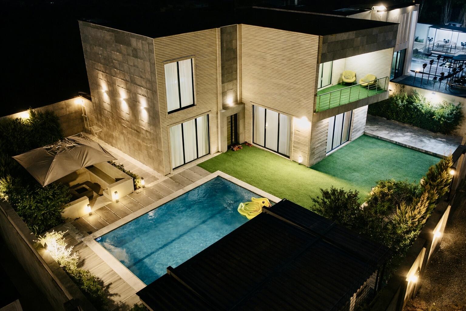 طراحی مدرن محوطه باغ ویلا در شب با نورپردازی استخر و چراغ‌های ایستاده