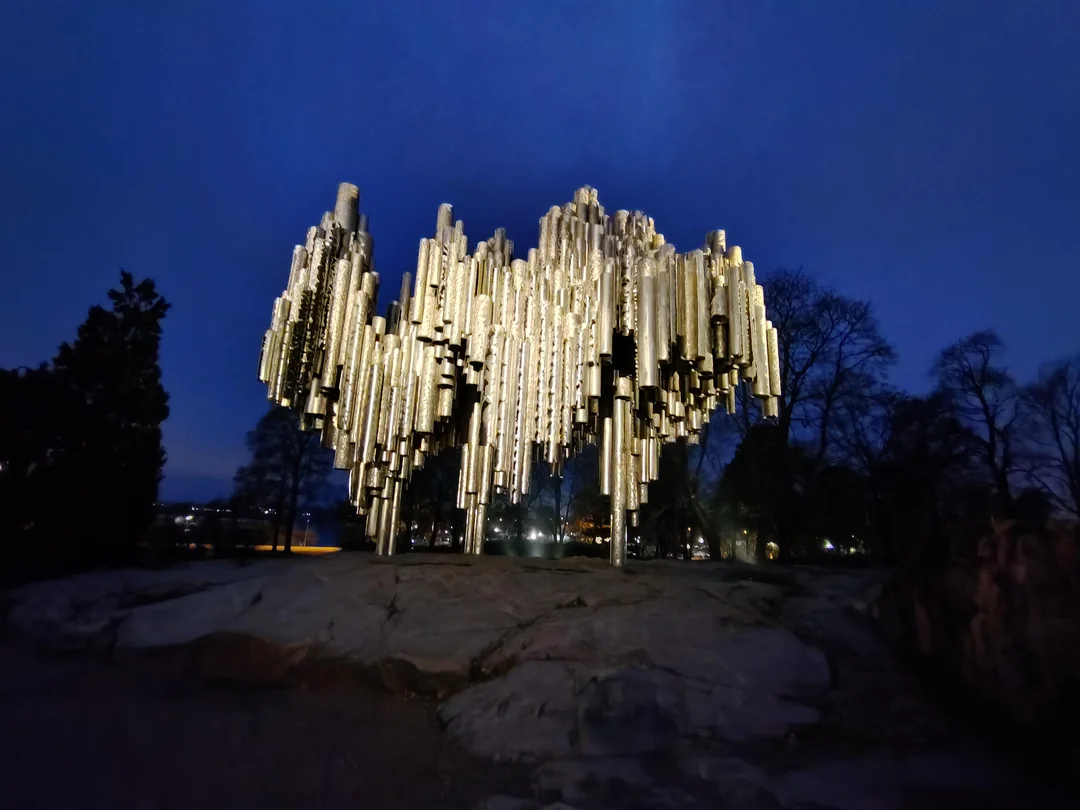 مجسمه فلزی لوله ای یادبود سیبلیوس روی صخره با نور گرم در پس زمینه آسمان آبی غروب در پارک سیبلیوس