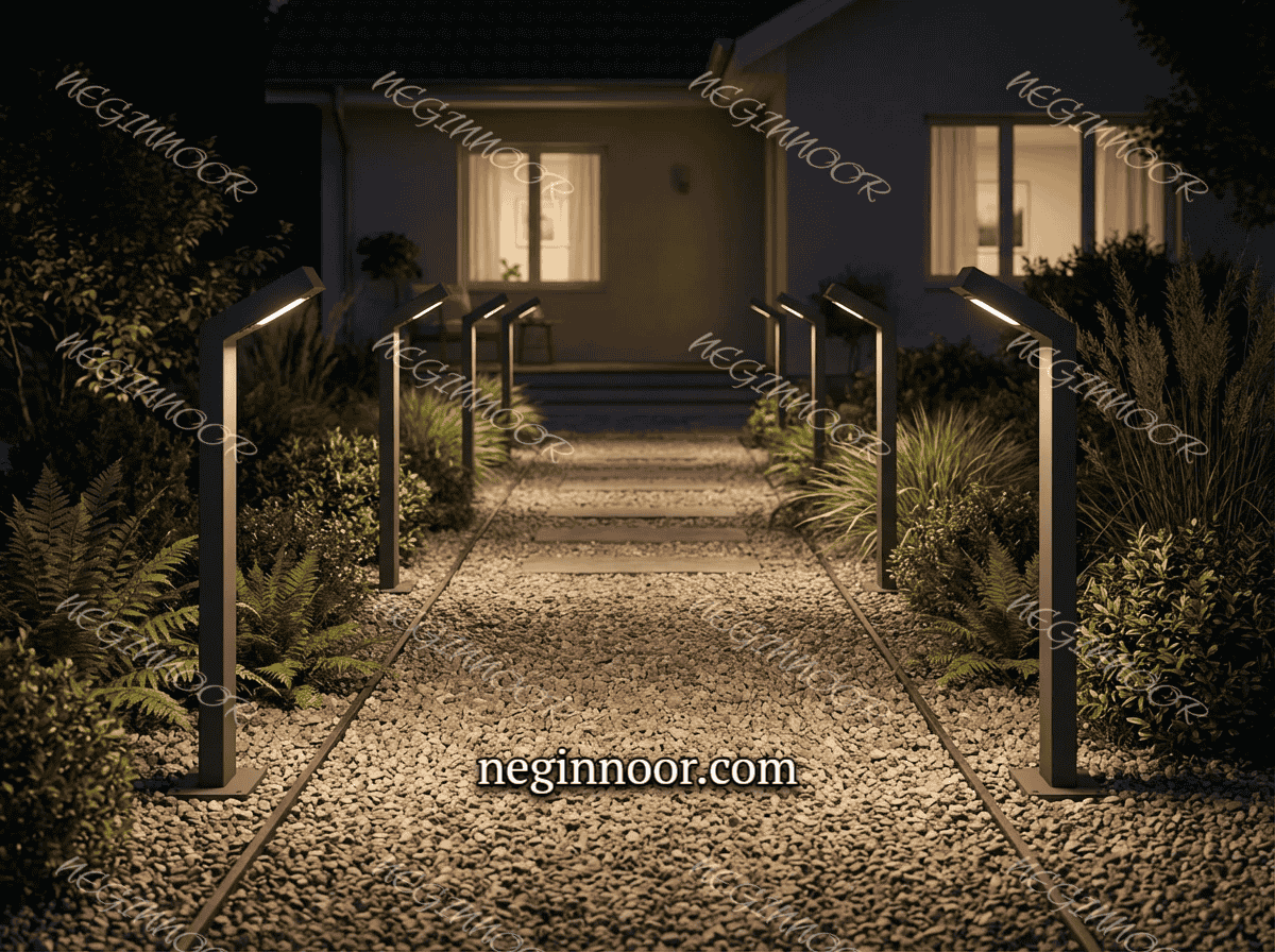 مسیر سنگریزه ای حیاط خانه که دو طرف آن با چراغ چمنی مدرن و پایه کوتاه روشن شده و نور ملایم روی کف و گیاهان اطراف باغچه می افتد