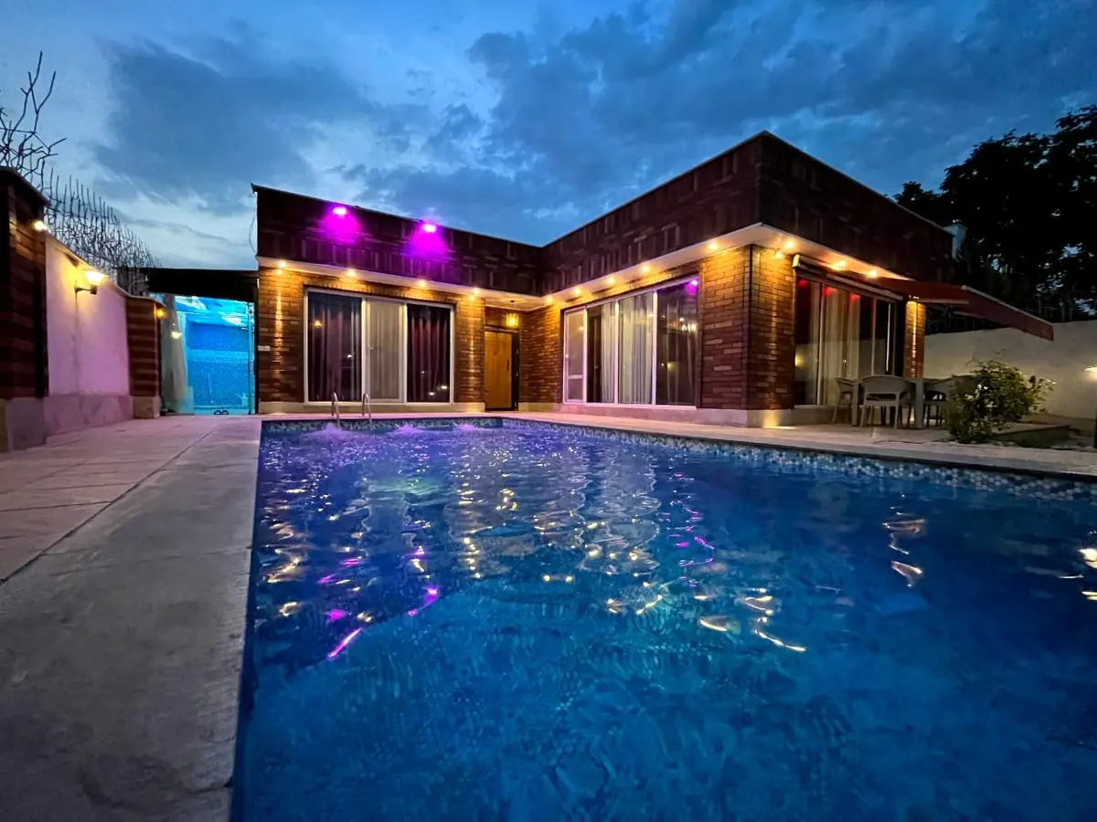 نورپردازی مدرن استخر و نمای آجری ویلا در شب با چراغ‌های خطی و هالوژن سقفی